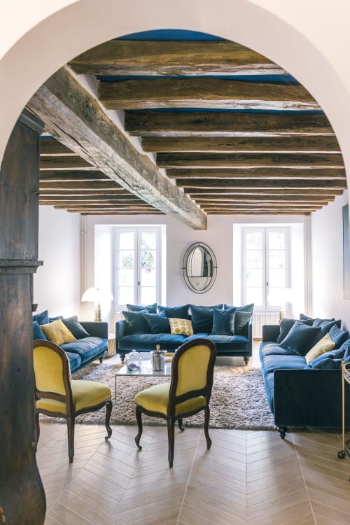 Élégant séjour du gîte Le Prieuré Du Preux avec poutres apparentes, canapés en velours bleu, fauteuils jaunes et