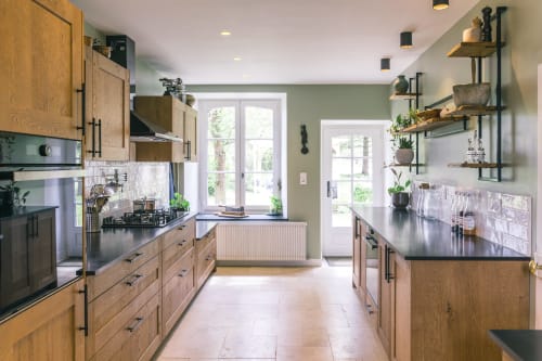 Cuisine moderne du Prieuré Du Preux avec meubles en bois, plan de travail noir, vue sur le jardin et étagères ouvertes