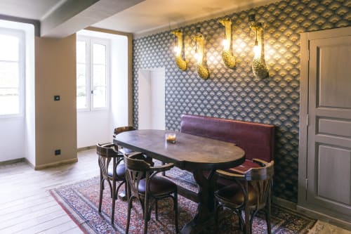 Élégante salle à manger du gîte Le Prieuré Du Preux avec papier peint à motifs, luminaires suspendus et banquette bordeaux.