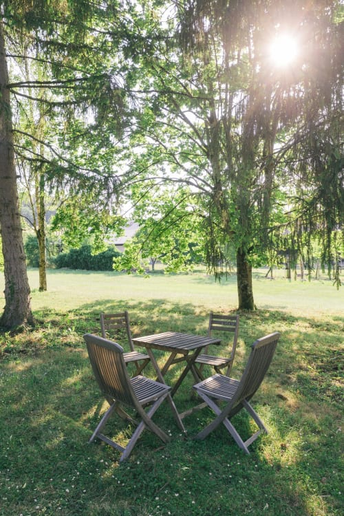 Table et chaises de pique-nique en bois dans le jardin du gîte Le Prieuré Du Preux, entourées d'arbres verts et d'une prairie ensoleillée
