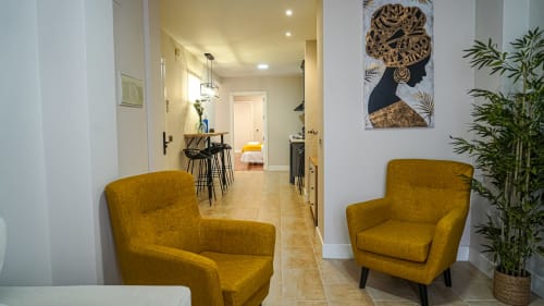 Pasillo moderno de apartamento en Mérida con sillas mostaza, plantas en macetas y acceso a vistas de la ciudad