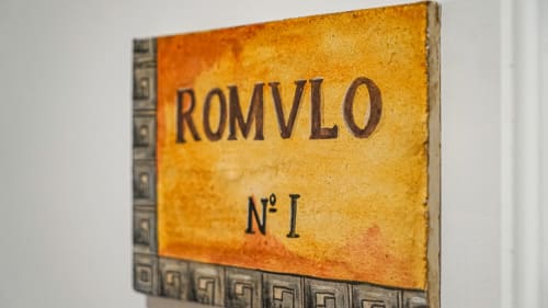 Placa amarilla rústica con inscripción 'ROMVLO Nº I' en apartamento Gestyp-AT de Mérida, con borde decorativo