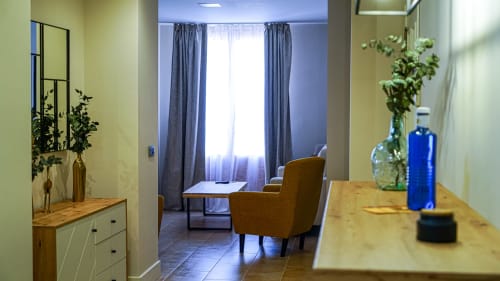 Departamento moderno en Mérida con sala abierta, silla mostaza, superficies de madera y vistas a la ciudad a través de cortinas