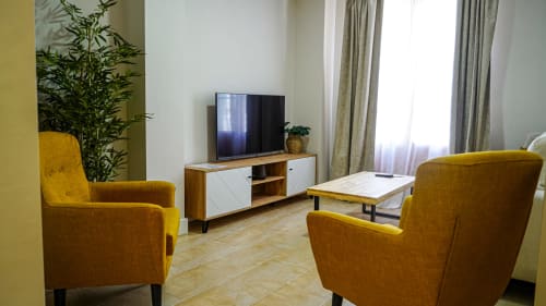 Sala de estar moderna en Mérida con sillones amarillos, mueble de televisión y vistas de la ciudad por ventanas con cortinas
