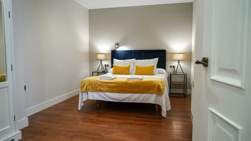 Dormitorio moderno con cabecera oscura, ropa de cama amarilla y pisos de madera en apartamento de Mérida