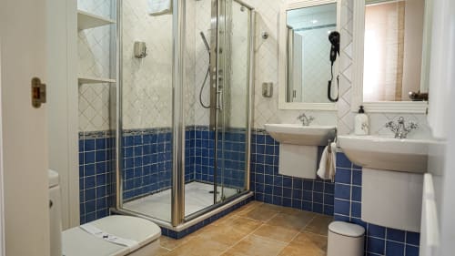 Baño moderno con doble lavamanos, ducha con mampara de cristal, azulejos azules y blancos en apartamento Gestyp-AT, Mérida