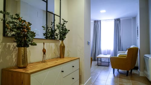 Moderno apartamento en Mérida con recibidor que cuenta con cómoda de madera, detalles dorados y vista de la ciudad a través de cortinas azules