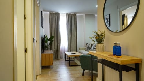 Moderno apartamento en Mérida con paredes amarillas, escritorio de madera, silla verde, plantas y espejo redondo con vistas a la ciudad