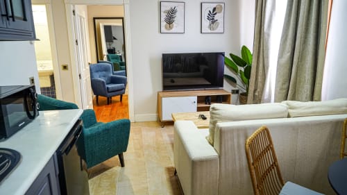 Moderno departamento en Mérida con living abierto, sofá crema, sillas teal, TV, cocina y arte botánico en pared.
