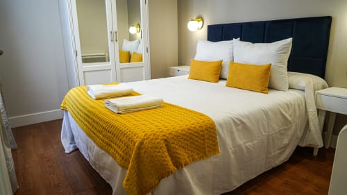 Elegante dormitorio en apartamento Gestyp-AT Mérida con vista a la ciudad, cama king con cabecero azul marino y acentos amarillos
