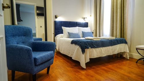 Moderno dormitorio en Mérida con cabecera tapizada azul, ropa de cama blanca, sillón y pisos de madera