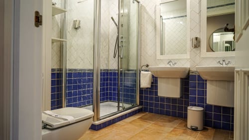 Baño moderno con doble lavamanos, ducha de vidrio, detalles en azulejos azules y piso de madera en apartamento de Mérida