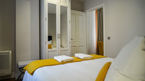 Habitación moderna del apartamento Gestyp-AT en Mérida con armario espejado, detalles amarillos y ropa de cama blanca