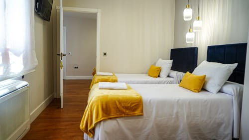 Moderna habitación doble en apartamento Gestyp-AT de Mérida con acentos amarillos, cabeceras oscuras y vista a la ciudad