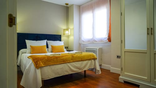 Moderno dormitorio del apartamento Gestyp-AT en Mérida con cabecero azul marino, detalles dorados y piso de madera