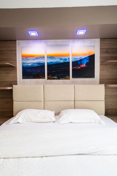 Dormitori de luxe modern a l'Hôtel Rocade amb capçalera crema, roba de llit blanca i tríptic posta de sol volcànic sobre el llit