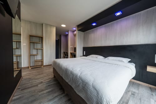 Habitació familiar moderna a l'Hôtel Rocade de Pamiers amb llit queen, capçal fosc, sòl de fusta i estanteries