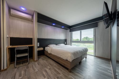 Habitació moderna a l'Hôtel Rocade de Pamiers amb llit queen, escriptori, TV i vistes a la ciutat per grans finestres