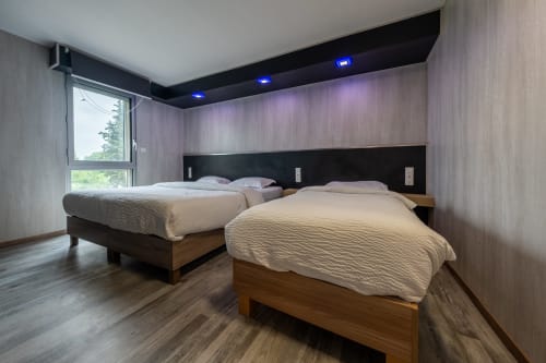 Habitació familiar moderna a l'Hôtel Rocade de Pamiers amb dos llits queen-size, detalls de fusta, il·luminació ambiental i vista a la ciutat
