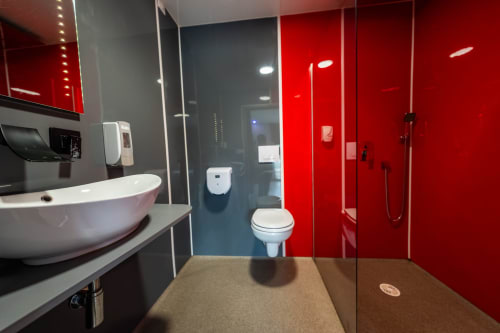 Bany modern a l'Hôtel Rocade de Pamiers amb dutxa de vidre vermell, lavabo blanc suspès, vàter i sòl de rajoles fosques