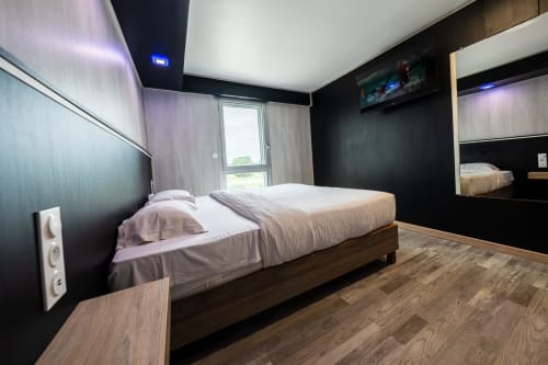 Habitació moderna de l'Hôtel Rocade amb llit queen, paret d'accent negra, TV de pantalla plana i vista de Pamiers