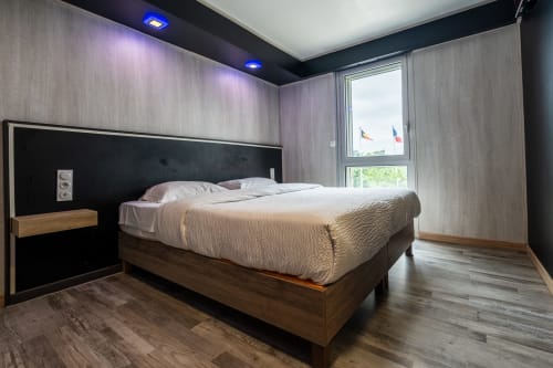Dormitori modern a l'Hôtel Rocade de Pamiers amb llit de fusta, capçal negre i grans finestres amb vistes a banderes