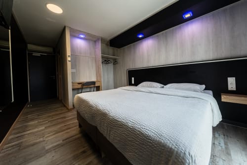 Habitació moderna a l'Hôtel Rocade de Pamiers amb llit queen, paret accent negra, mobles de fusta i il·luminació blava