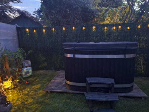 Baignoire thermale illuminée dans le jardin du gîte La Cour d'Hortense, Sailly-Flibeaucourt, avec clôture lierre et éclairage d'ambiance