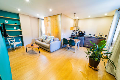 Modern open-plan living room at Gites bo BnB in Saint-Romain with turquoise accent wall, sofa, wooden flooring and kitchen
