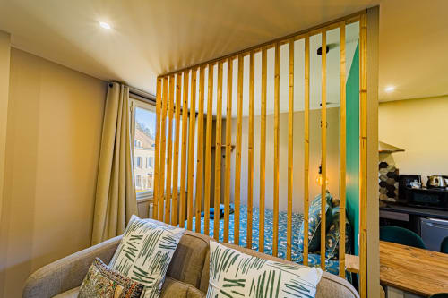 Modern bedroom at Gites bo in Saint-Romain with yellow wood room divider, grey armchair, and city view through window