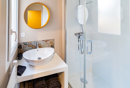 Modern bathroom at Gites bo B&B in Saint-Romain with round mirror, white vessel sink, and glass shower enclosure