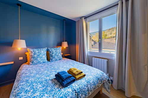 Modern blue bedroom at Gites bo in Saint-Romain with mountain views, pendant lights, patterned bedding, and welcome towels