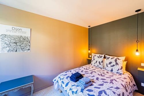 Modern bedroom at Gites bo in Saint-Romain with patterned bedding, Dijon map, warm lighting, and blue accent wall