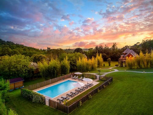 Aerial view of Domaine De Campagnac in Carsac-Aillac with pool, manicured grounds, and treehouse at sunset