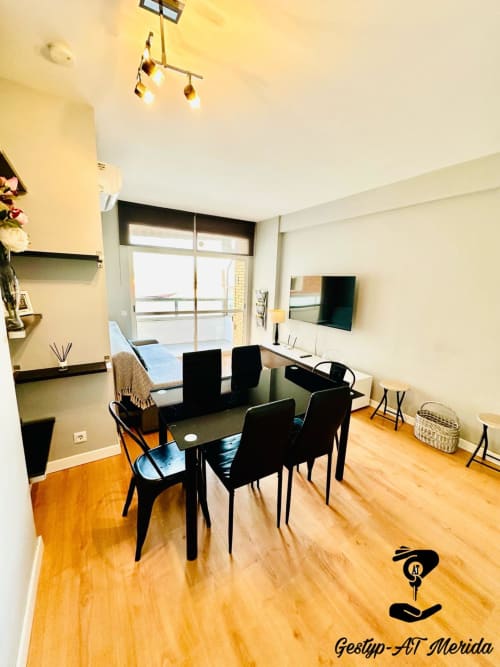 Apartamento moderno en Gestyp-AT Mérida con mesa de comedor, sillas negras, pisos de madera y balcón con vista a la ciudad
