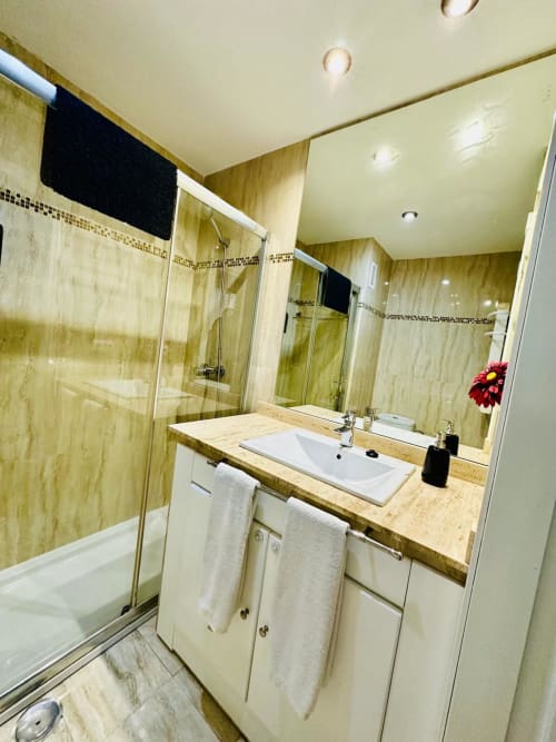 Baño moderno en apartamento de Mérida con azulejos de mármol, lavamanos doble y ducha de cristal templado