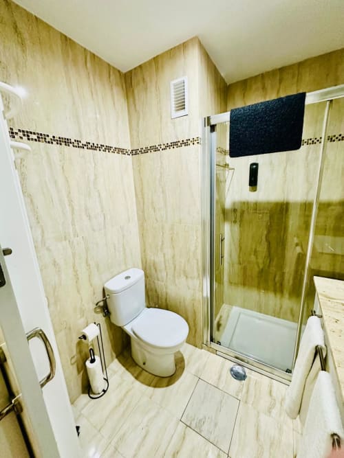 Baño moderno con azulejos de mármol, cabina de ducha de cristal e inodoro blanco en apartamento Gestyp-AT, Mérida
