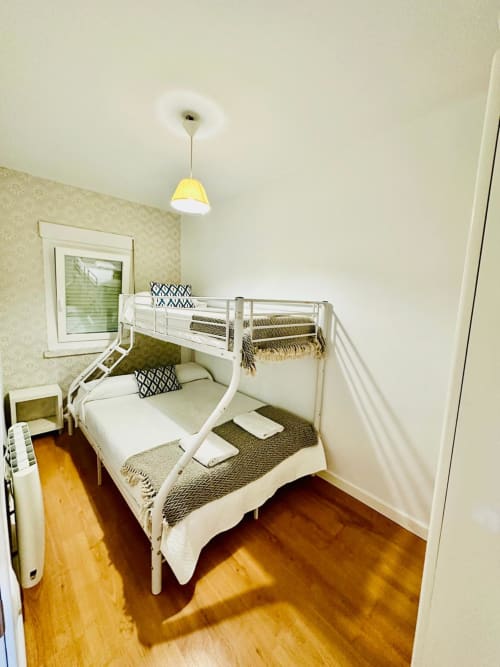 Luminosa habitación de huéspedes con camas literas blancas, piso de madera y lámpara colgante amarilla en apartamento Gestyp-AT en Mérida