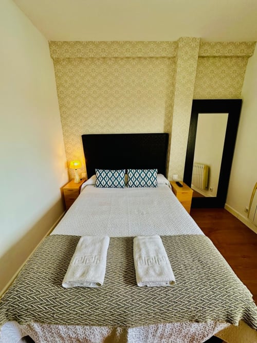 Dormitorio moderno en apartamento Gestyp-AT Mérida con cabecero negro, ropa de cama estampada, toallas enrolladas y vistas a la ciudad