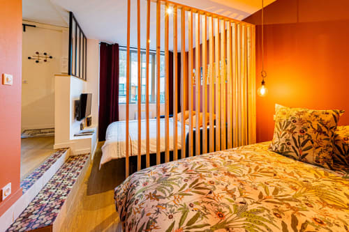 Chambre lumineuse aux murs orangés, cloison en bois, parure florale et salle de bain attenante aux Gîtes bo à Saint-Romain.