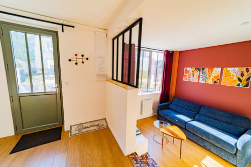 Salon chaleureux aux Gites bo à Saint-Romain avec canapé bleu, parquet, mur d'accent rouge et grandes fenêtres