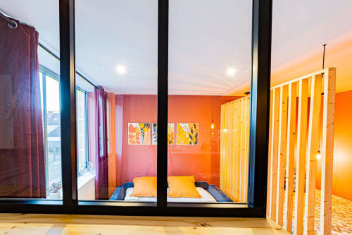 Chambre moderne aux Gites bo à Saint-Romain, murs orange vibrants, coussins jaunes et baies vitrées