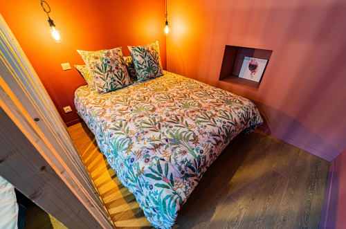 Chambre colorée de l'appartement Le Boisé aux Gîtes bo, Saint-Romain, avec parure de lit motifs, murs orange chauds, luminaires suspendus