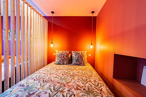Chambre lumineuse à l'appartement Le Boisé, Saint-Romain, avec murs orange vibrants, literie à motifs et luminaires suspendus.
