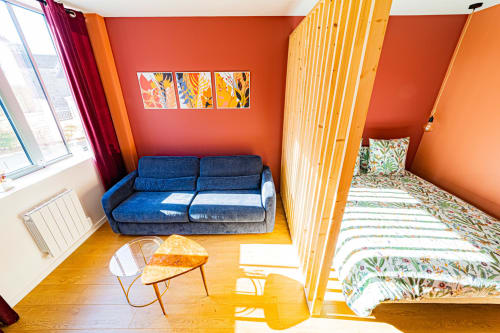 Lumineux studio aux Gites bo avec canapé bleu, claustra bois, murs orangés et linge fleuri à Saint-Romain