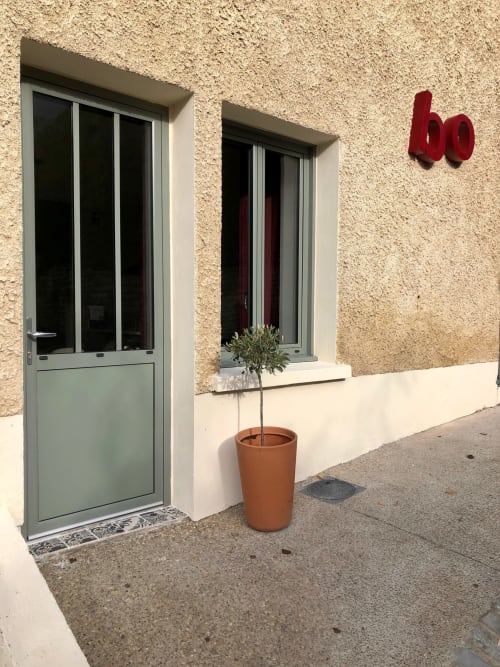 Gites bo entrance in Saint-Romain with gray door, potted plant, and red house number sign