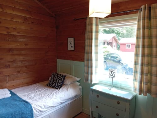 Cozy cabin bedroom at Grouse Lodge, Dunoon with wooden walls, single bed, green dresser, and countryside views