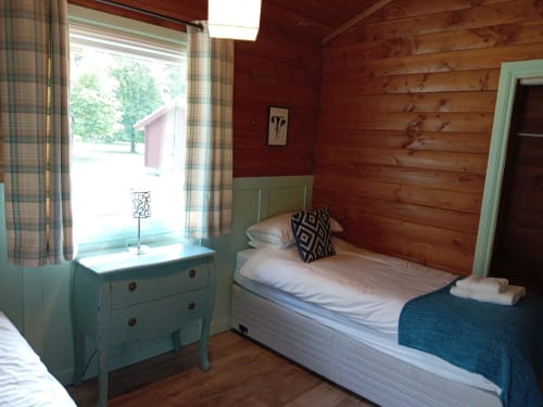 Cozy bedroom at Grouse Lodge in Dunoon with red log walls, green dresser, and natural daylight from window