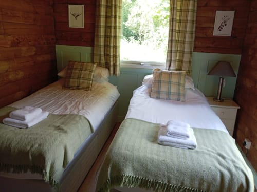 Twin bedroom at Grouse Lodge in Dunoon with tartan furnishings, wood paneling, and countryside views
