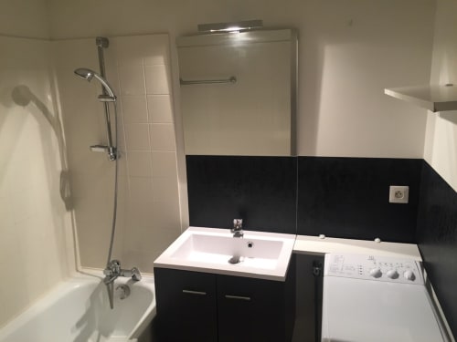 Modern bathroom with black and white tile, white sink vanity, shower, and washing machine in Le Charmant Zola apartment,